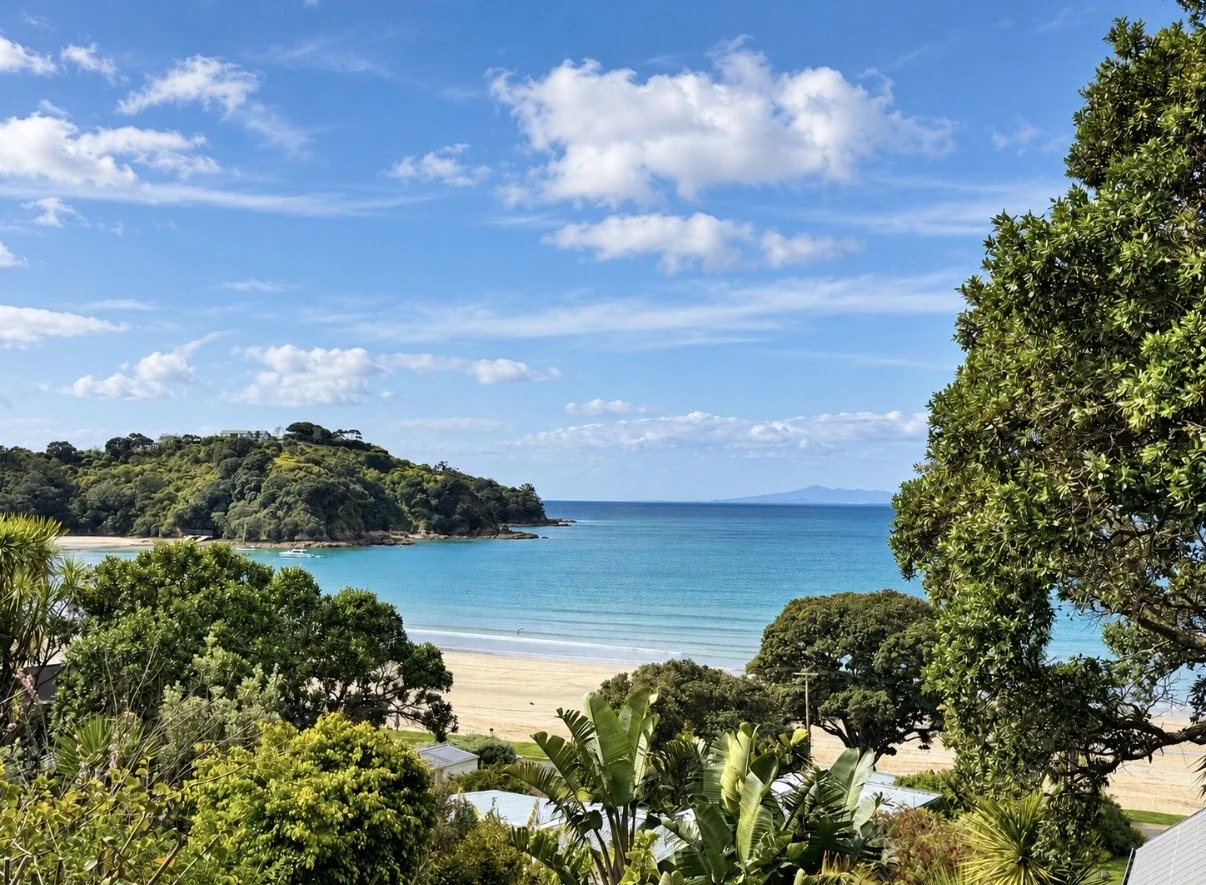A scenic view of a sandy beach with turquoise water, green trees, and a partly cloudy sky.