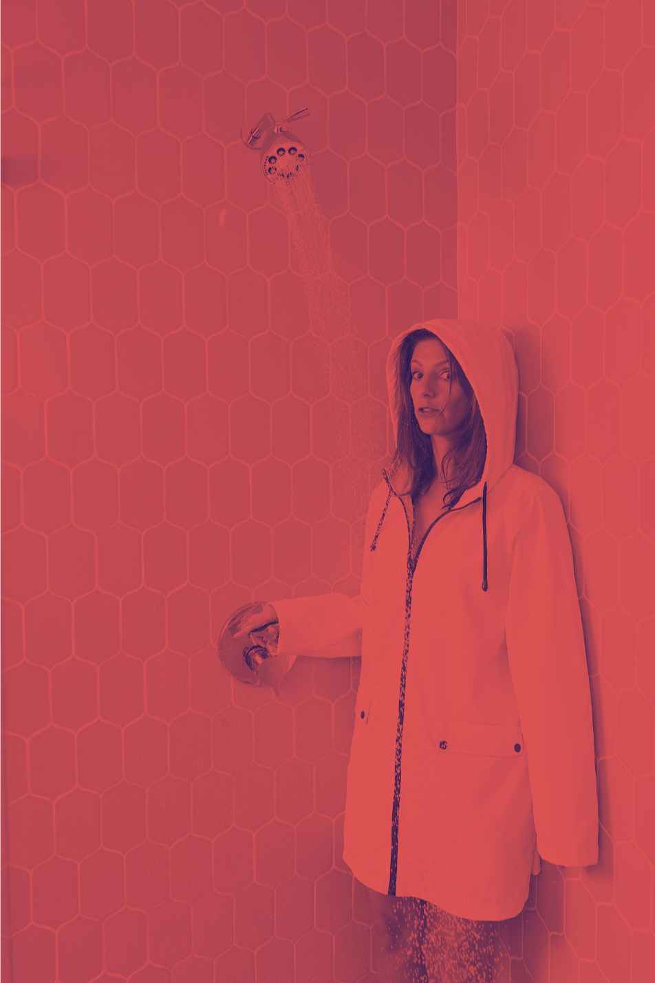 Clara Bijl in a hooded jacket standing under a showerhead on a tiled wall.