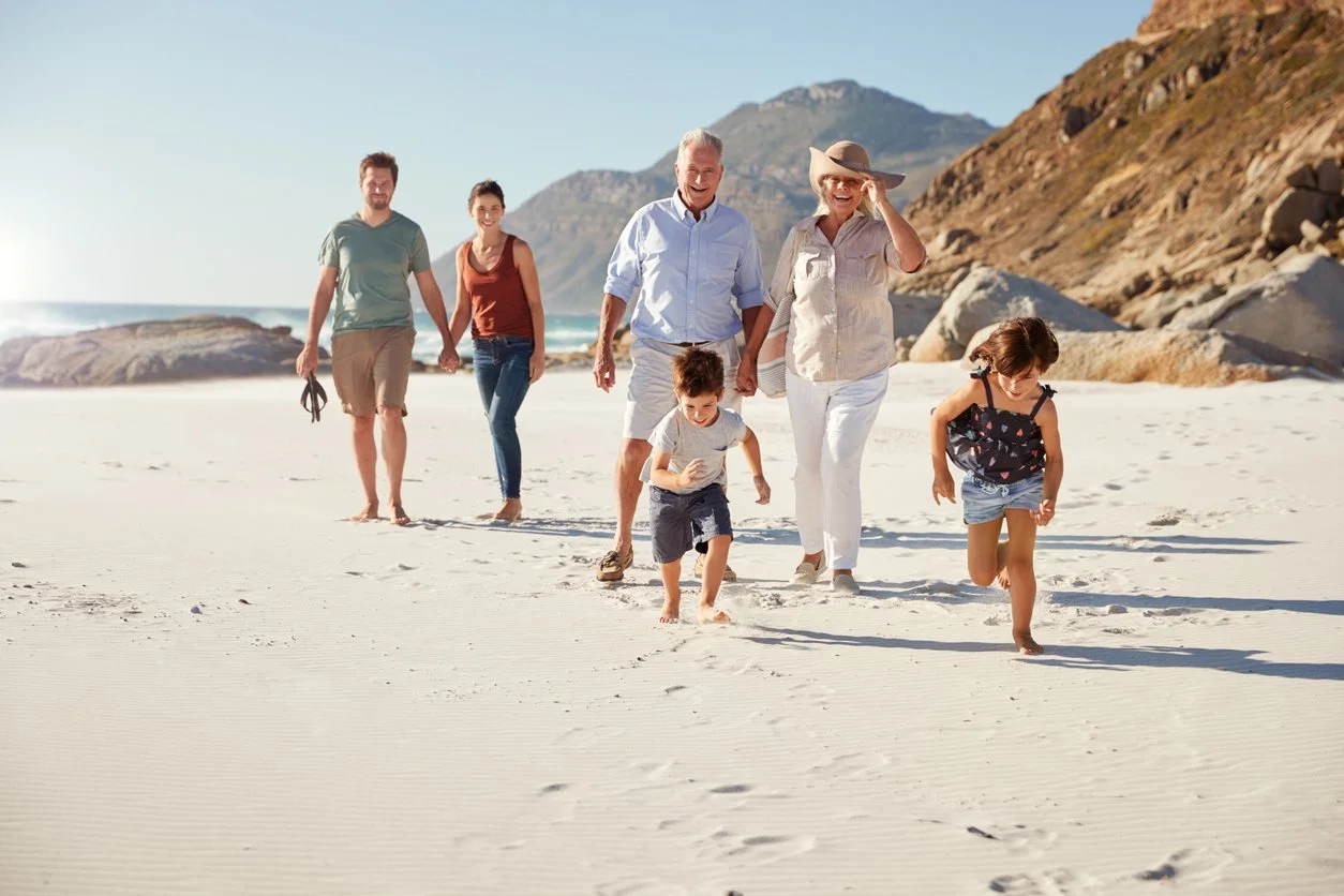 Family of six walking on a sandy beach with cliffs in the background, enjoying a sunny day.