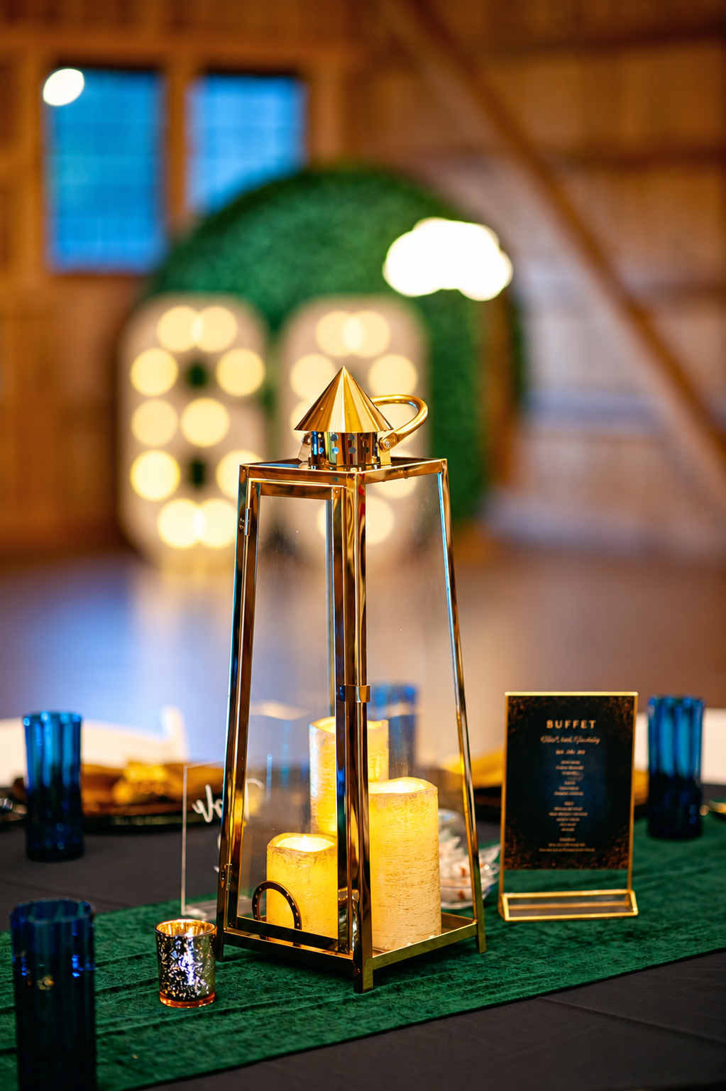 Gold lantern centerpiece with candlelight and emerald accents at a 60th birthday celebration.