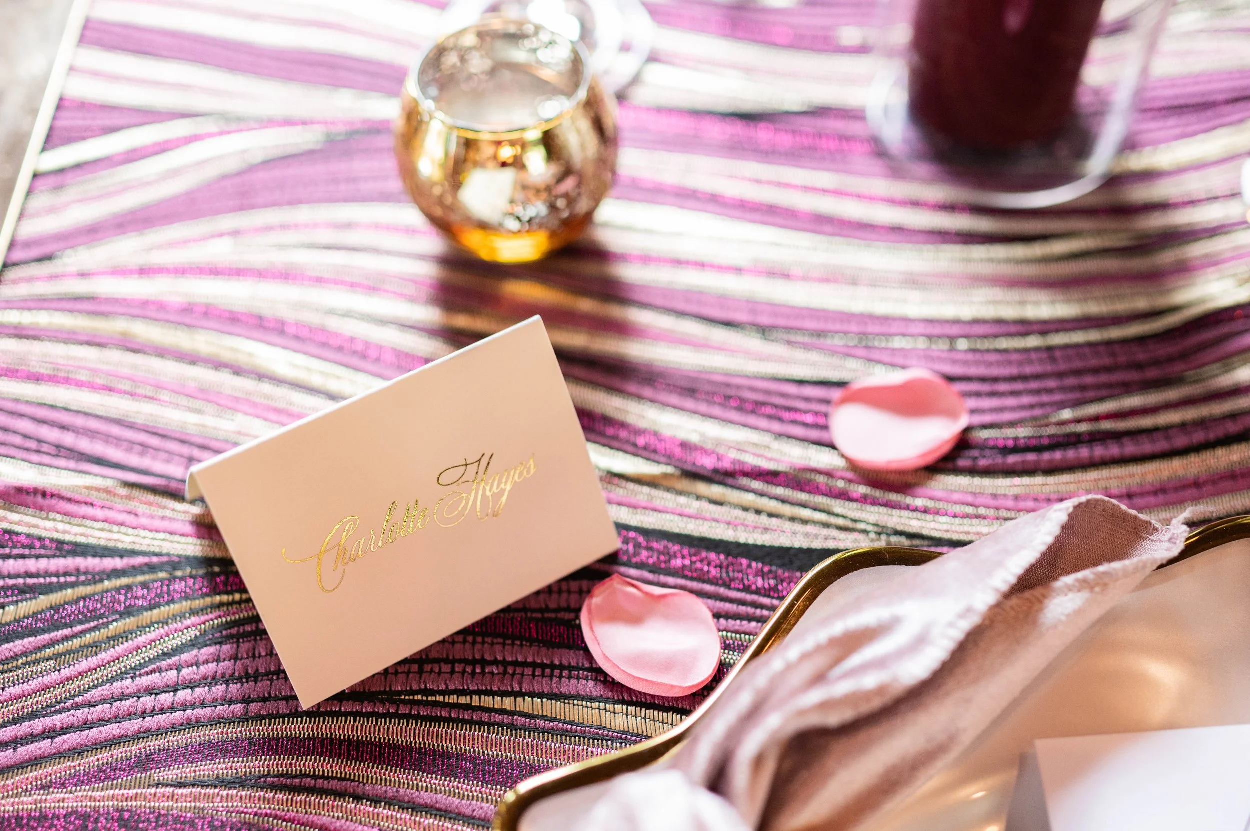 Personalized wedding place card styled with rose petals and layered table details.