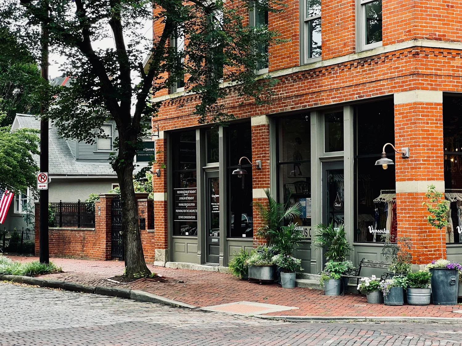 Brick corner storefront with large windows and potted plants along the sidewalk