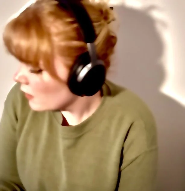 A woman with red hair wearing large black headphones, facing sideways, in a green shirt.