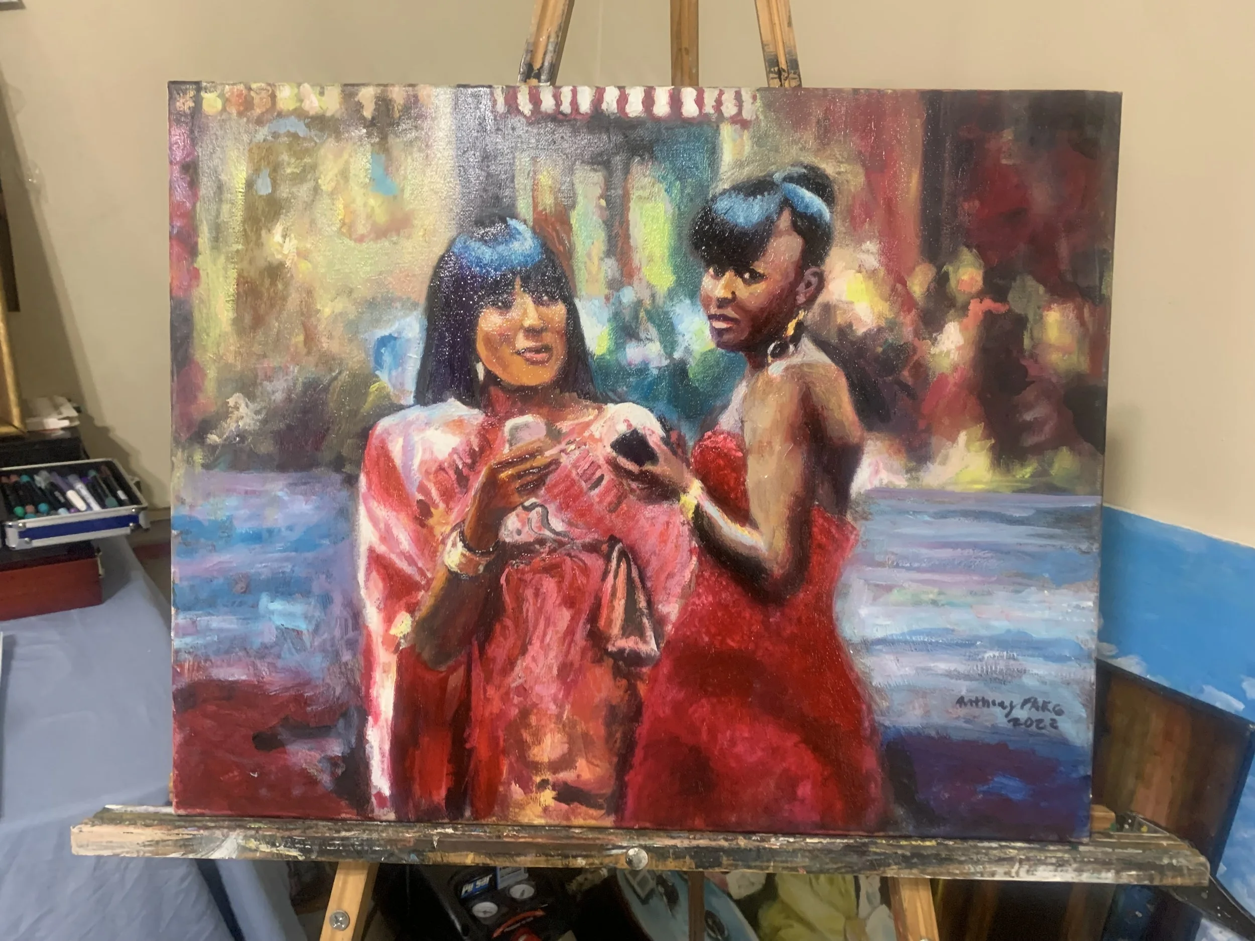 A colorful impressionist-style painting of two women with dark hair and sunglasses, standing close together. One woman is smiling and holding a glass, while the other has a serious expression. The background features vibrant abstract colors suggesting an outdoor setting.