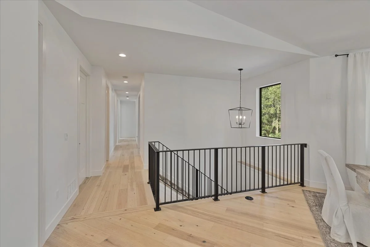 Updated upstairs hallway featuring light hardwood floors, white walls, black metal railings and a modern hanging light fixture