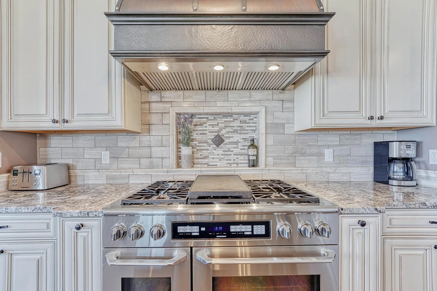 Custom kitchen featuring a stainless steel double oven range, decorative metal range hood, granite countertops, and detailed tile backsplash