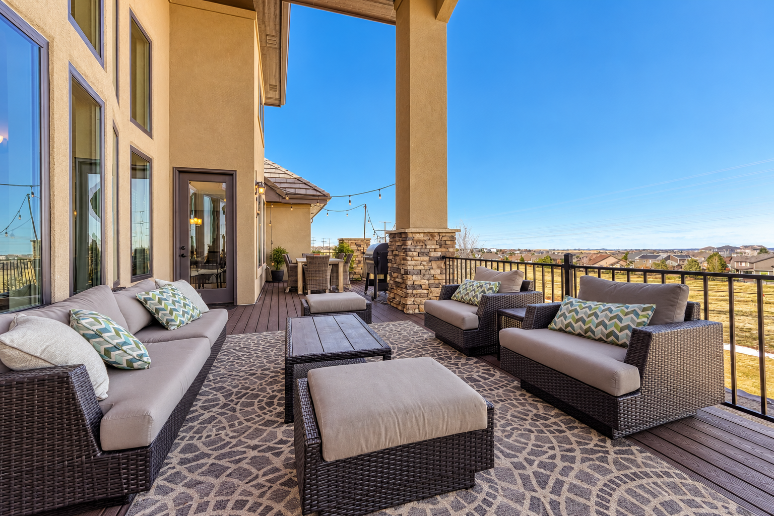 Luxury patio retreat with wicker lounge furniture, cushioned seating, patterned area rug, stone columns and scenic views