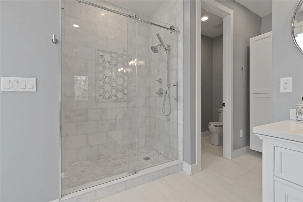 Modern bathroom featuring a spacious walk-in shower with marble-look tile, decorative tile accent, sliding glass doors, and chrome fixtures.