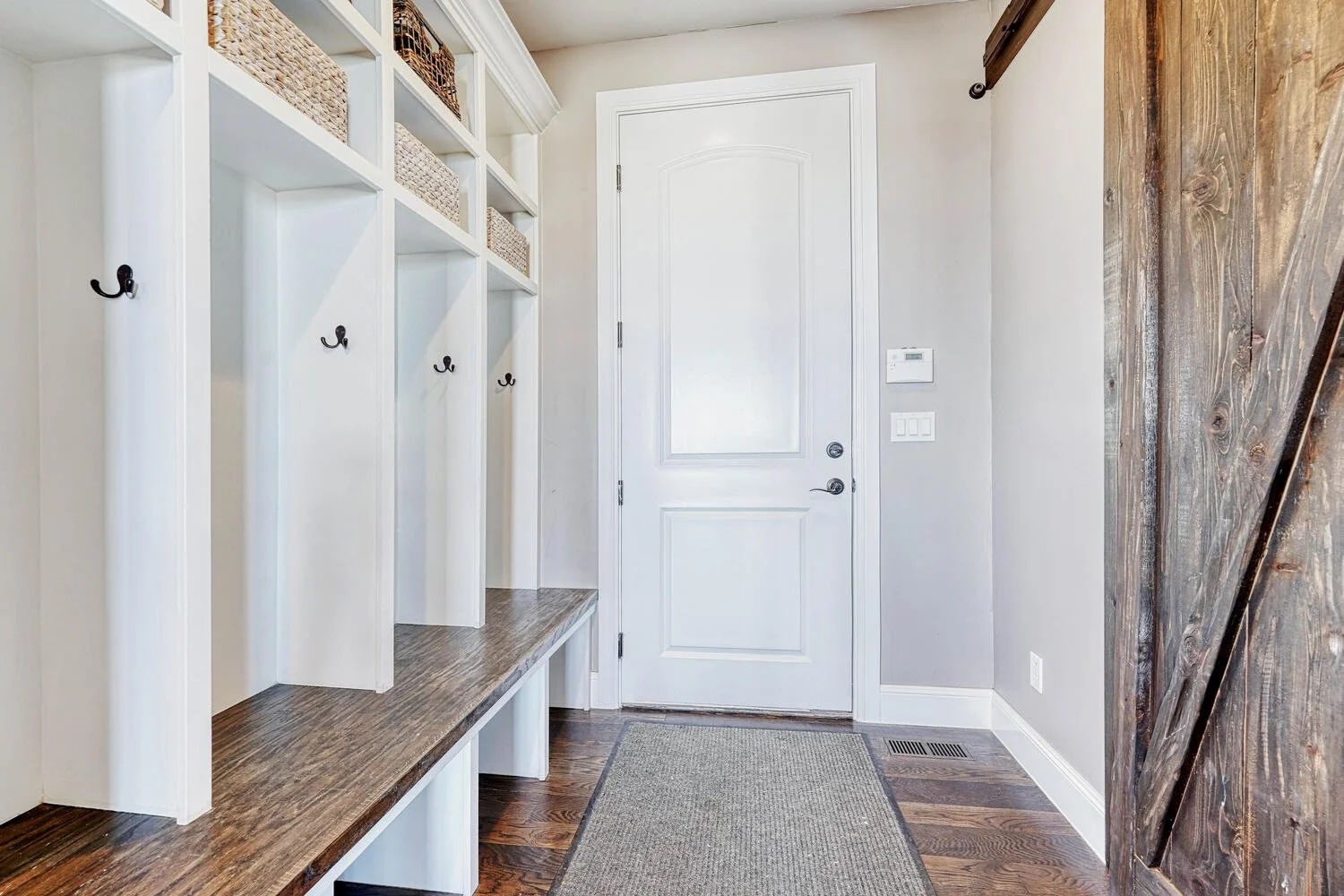 Custom mudroom featuring whitte built in storage cubbies, wood bench seating, woven baskets, hooks and hardwood flooring