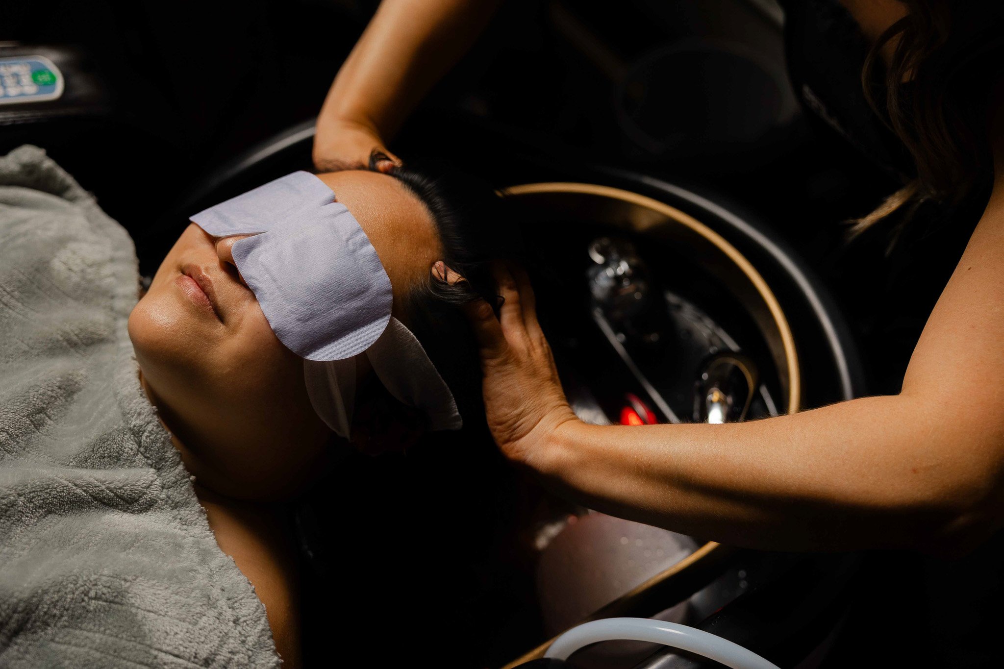 Person lying down with a cloth over eyes, receiving a massage or facial treatment, in a spa or salon setting.