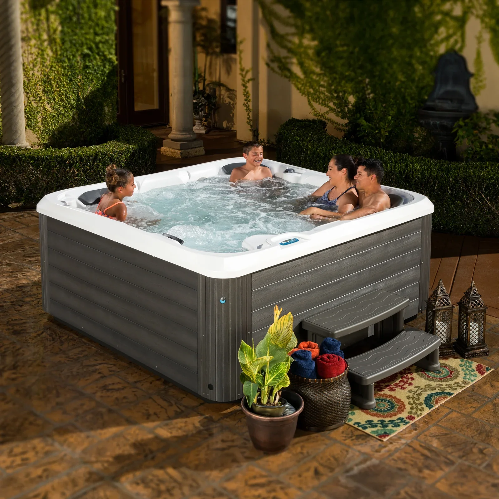 Family relaxing in a bubbling outdoor hot tub on a landscaped patio