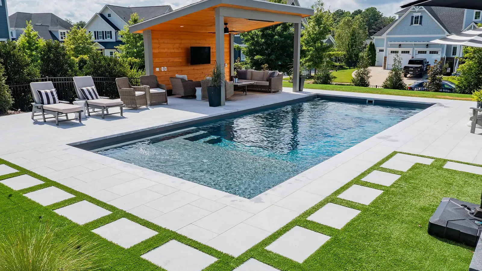Modern backyard with a rectangular swimming pool, covered outdoor lounge, patio seating, and landscaped lawn