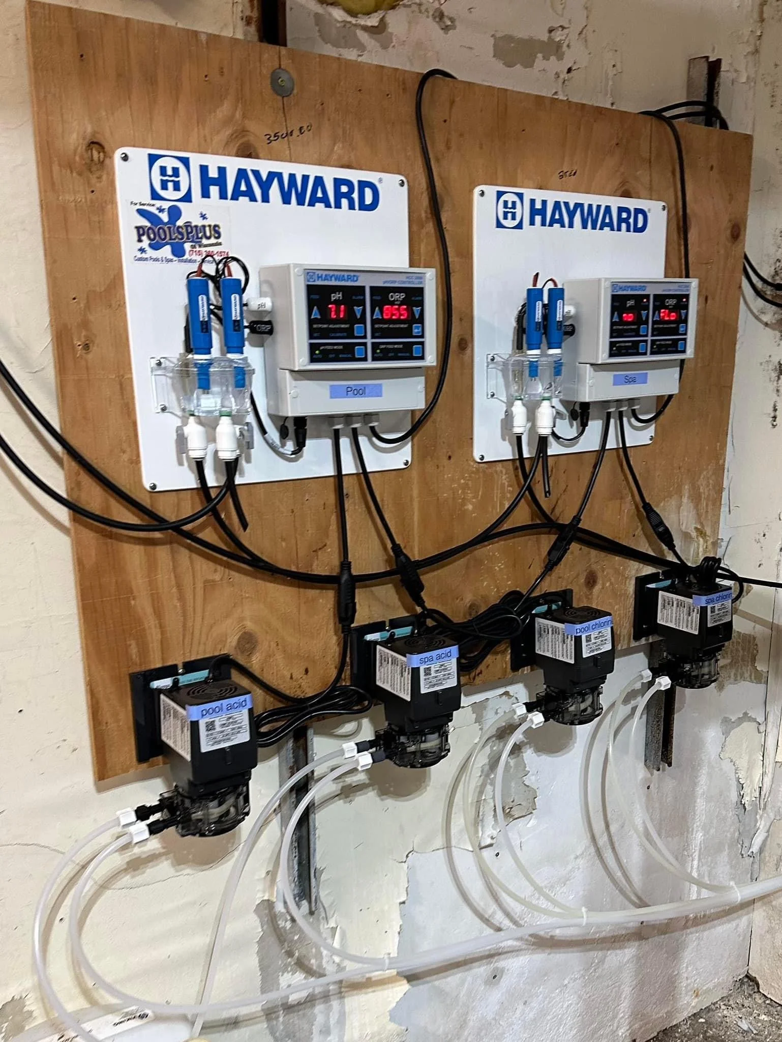 Hayward pool and spa chemical automation system with digital pH and ORP controllers, dosing pumps, chemical sensors, and tubing mounted on a plywood panel.