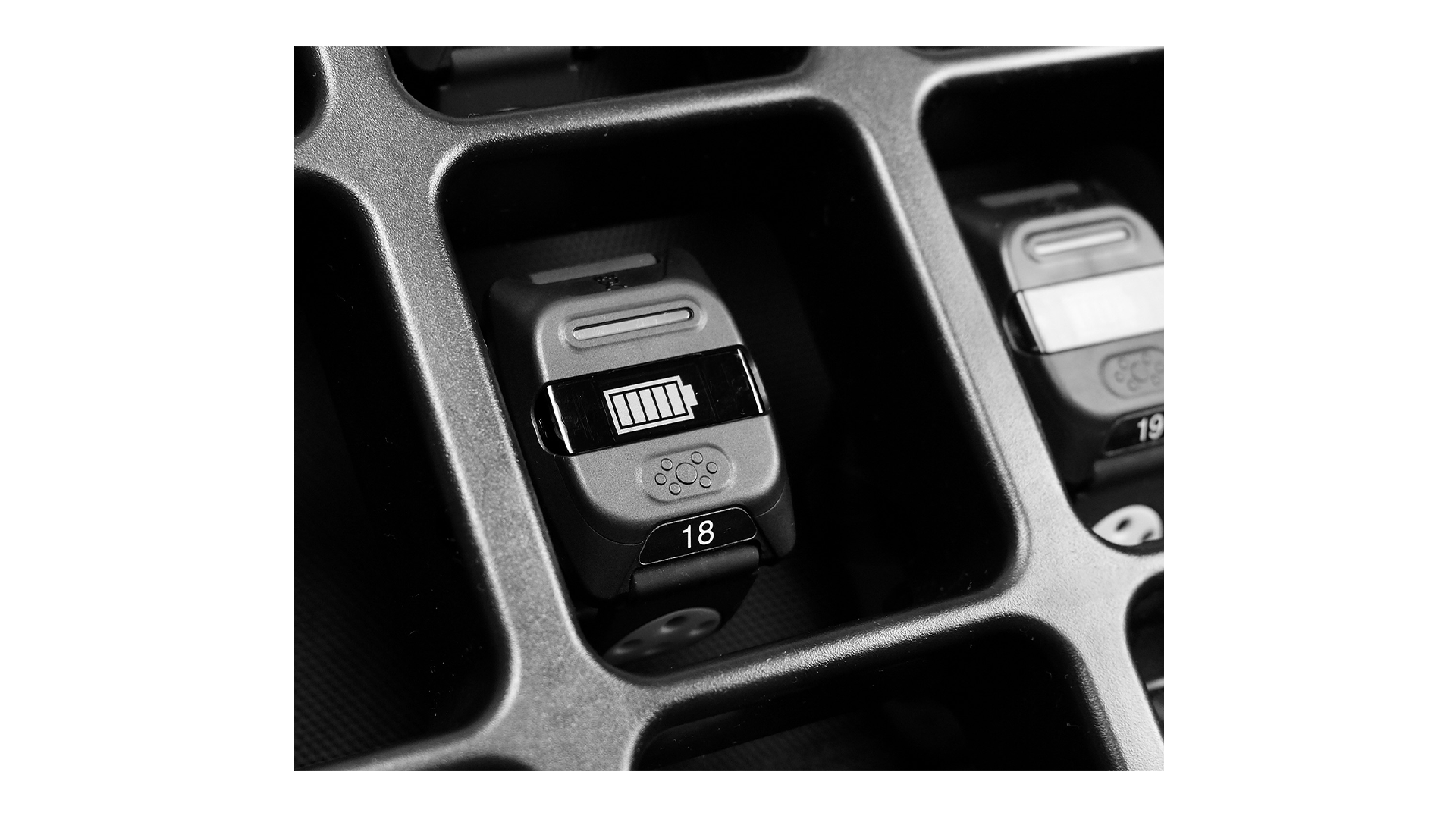 Close-up of a digital fitness tracker in a charging case with a battery icon and the number 18, stored in a compartment.
