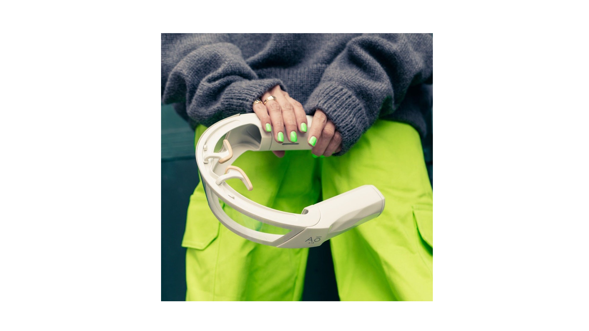 Person wearing a gray sweater and bright neon yellow pants holding a white virtual reality headset.