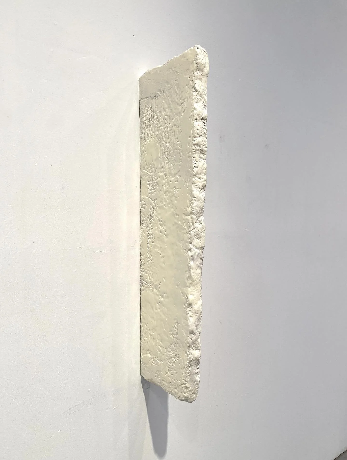 A white, textured, zigzag-shaped sculpture mounted on a white wall.