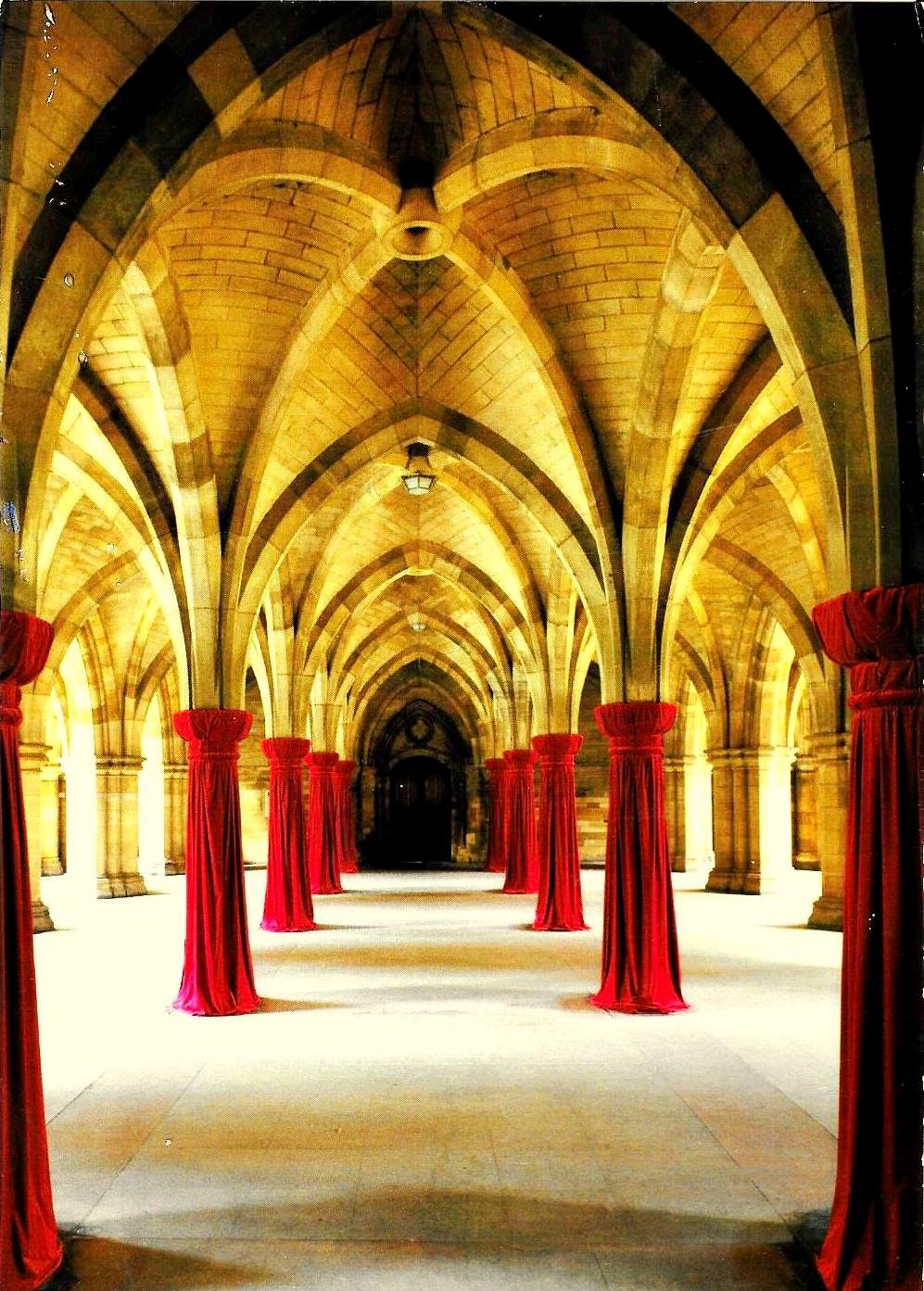 Interior of a grand hallway with Gothic-style pointed arches, illuminated with warm lighting, lined with tall red velvet curtains on columns.