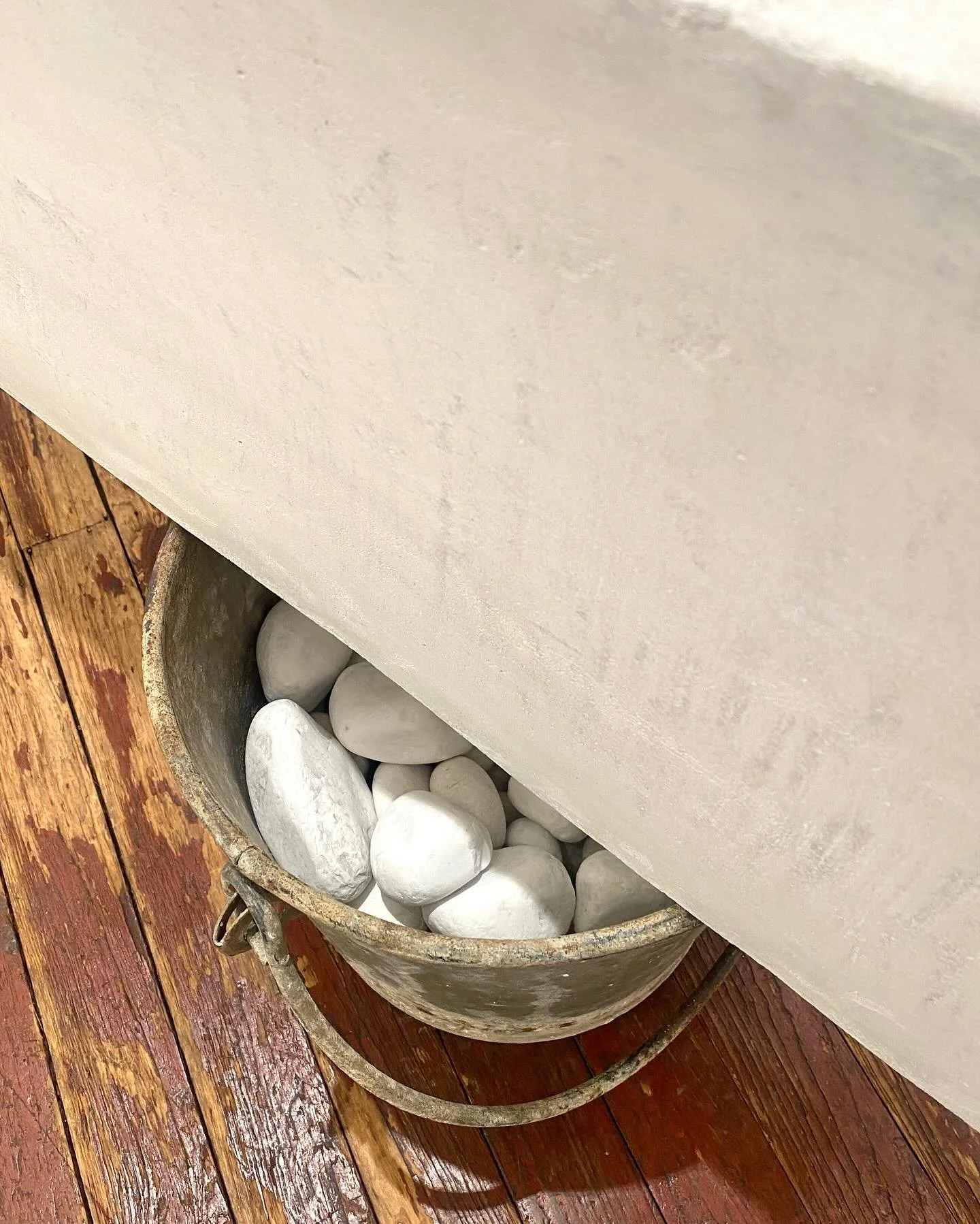A metal container filled with white decorative stones placed on a wooden surface next to a beige-colored wall.