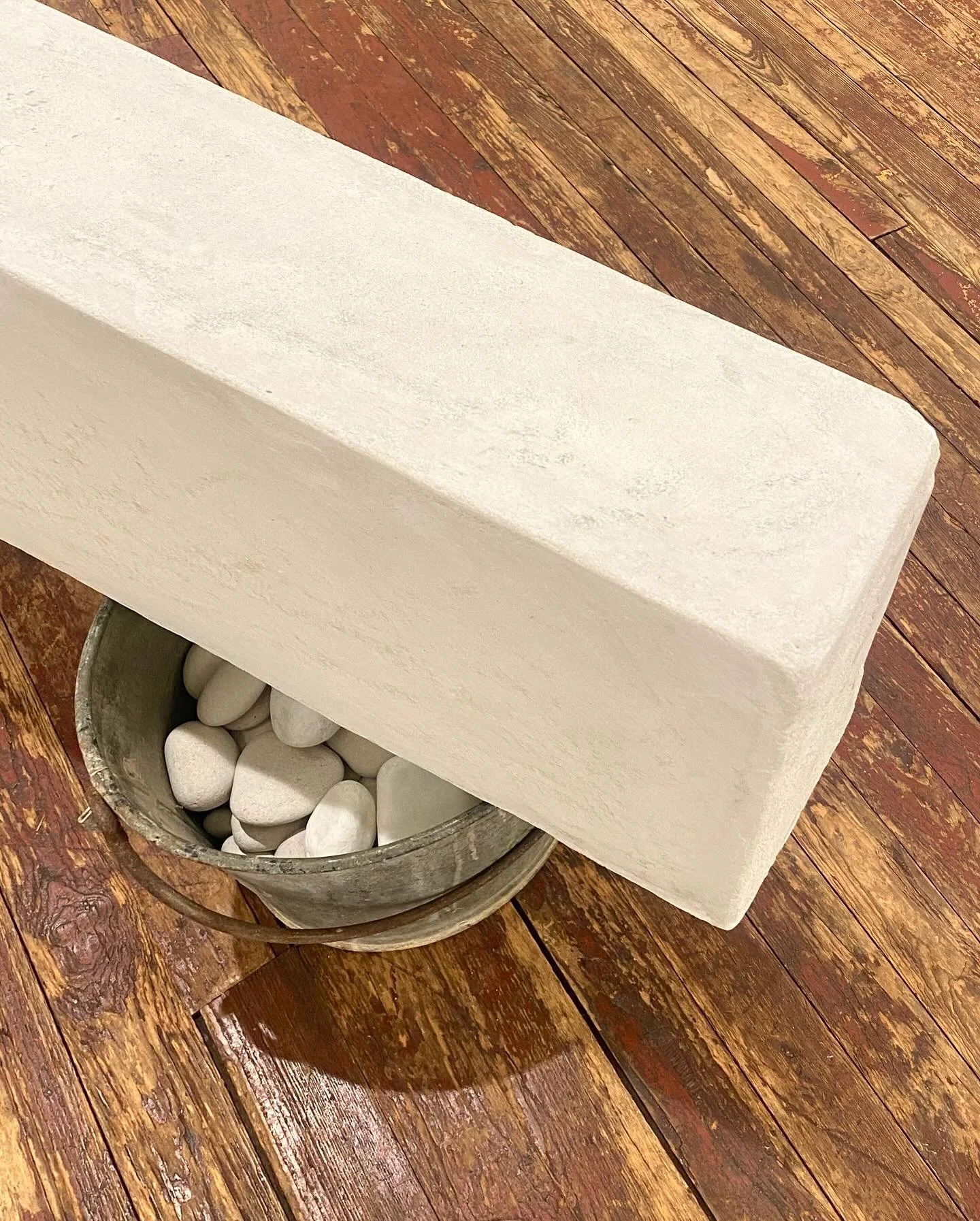 A white rectangular stone fountain with rounded edges, filled with white stones, on a wooden floor.