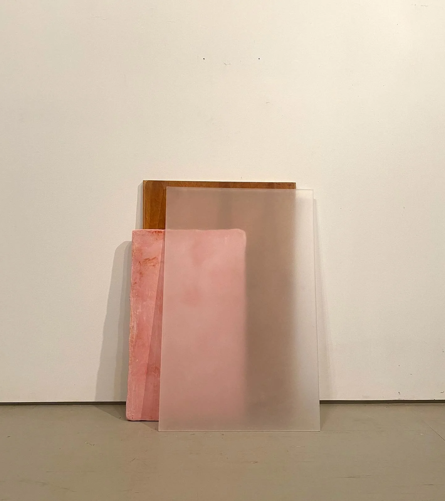 Three vertically aligned rectangular sheets leaning against a plain white wall. The left sheet is pink with a marbled texture, the middle sheet is matte pink, and the right sheet is transparent.