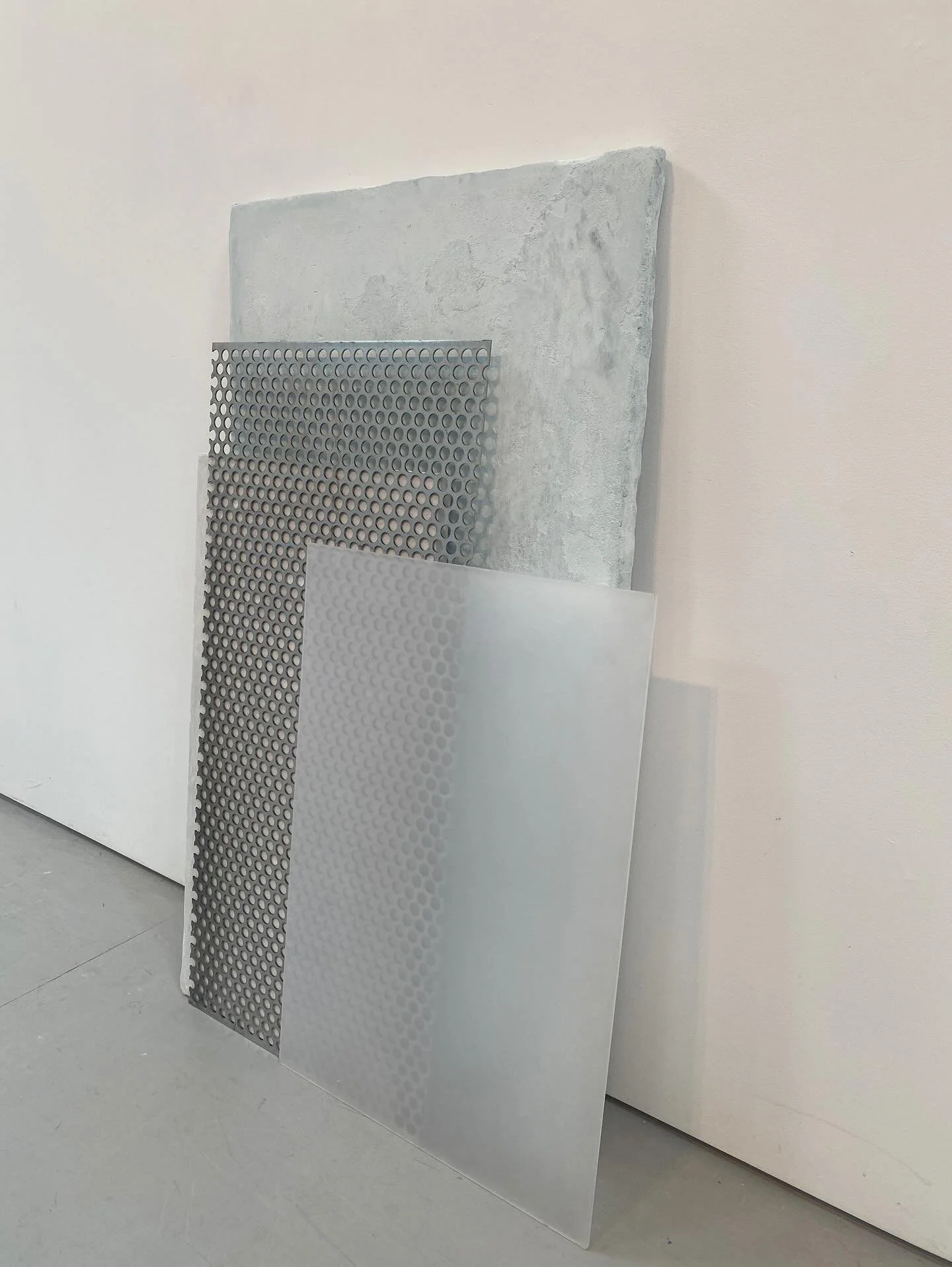 Four metal sheets with circular patterns leaning against a white wall.