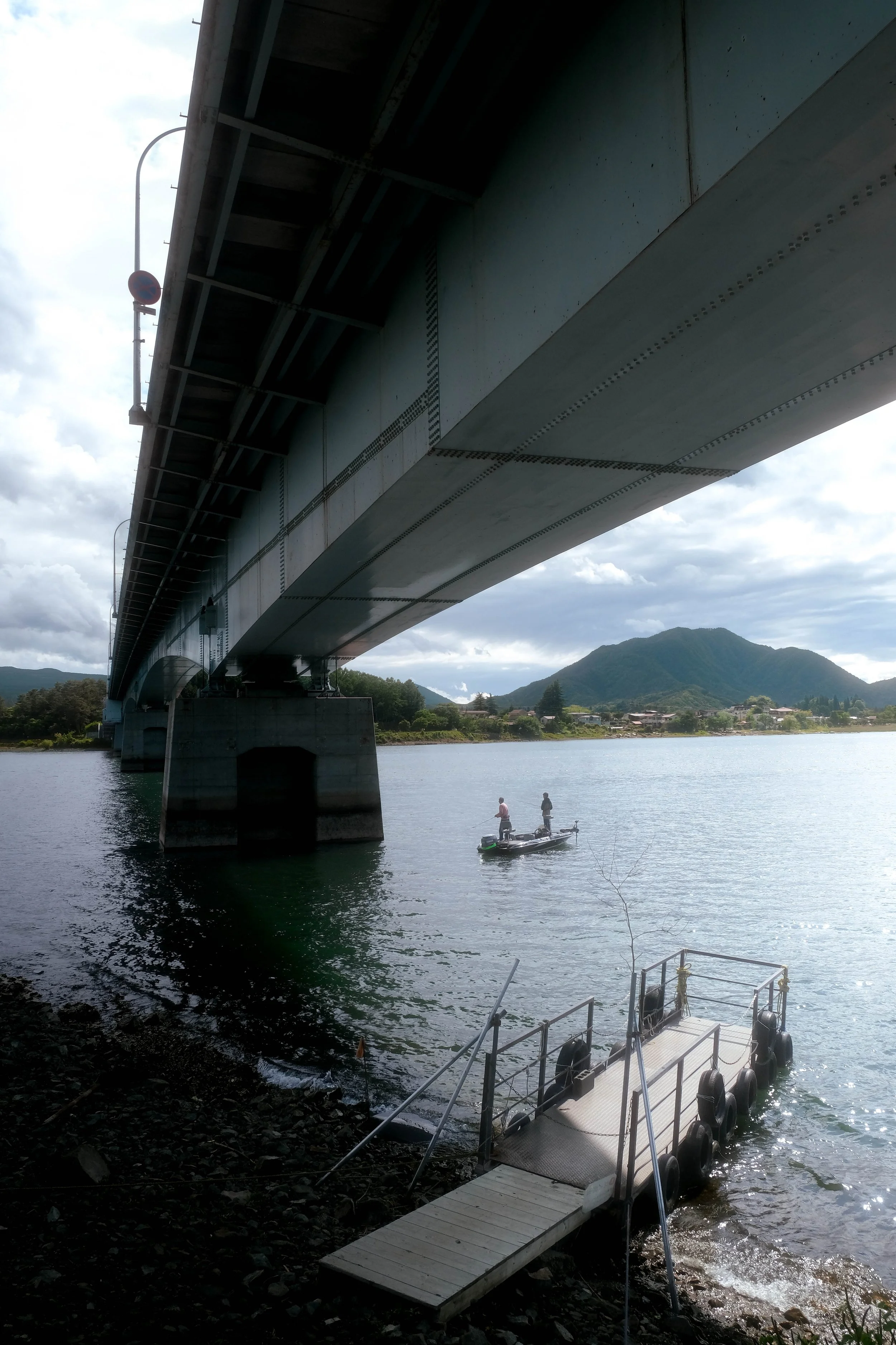 View of a bridge over a river with a small boat carrying two people in the water, and a mountain in the background.
