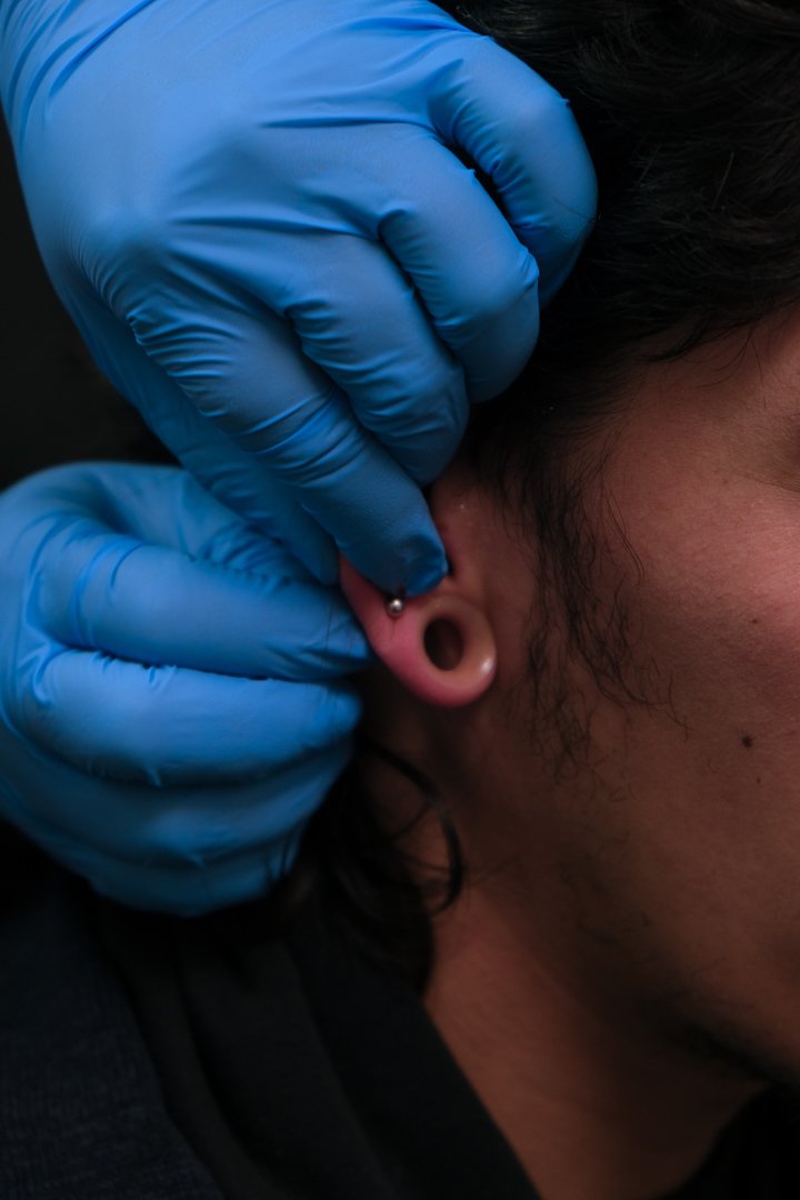 A person with dark hair getting an ear piercing by a professional wearing blue latex gloves.