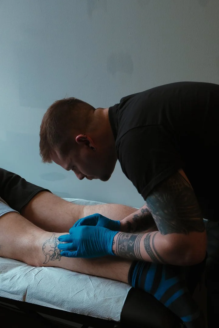 Tattoo artist wearing blue gloves creating a tattoo on a person's forearm in a studio.