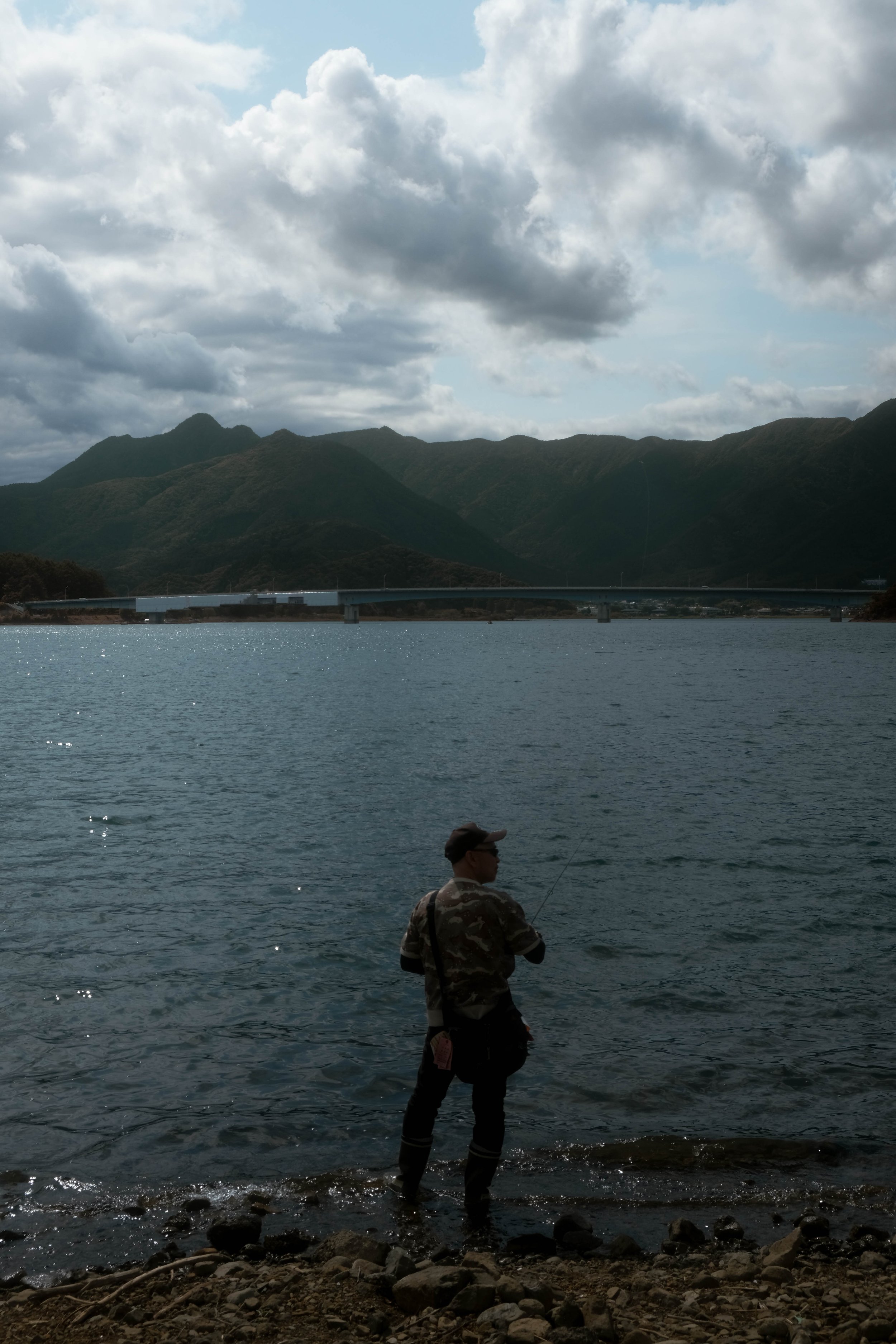 A person fishing in a body of water with mountains and a cloudy sky in the background.