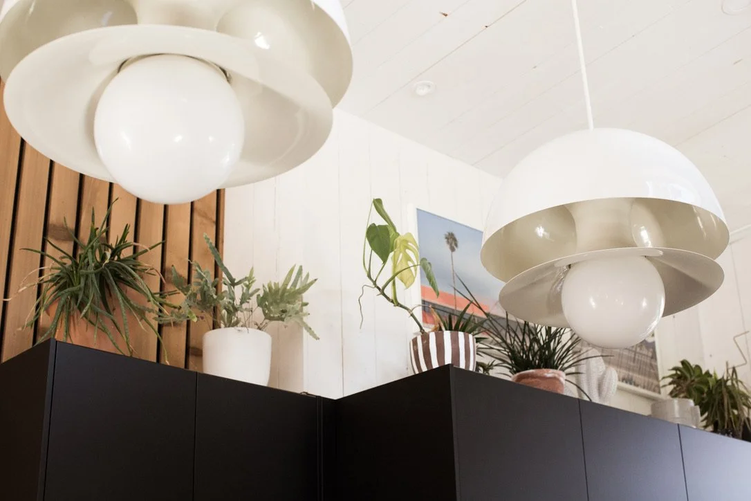 Ceiling lights with layered round shapes, potted plants on top of a black cabinet, artwork on white wooden wall.