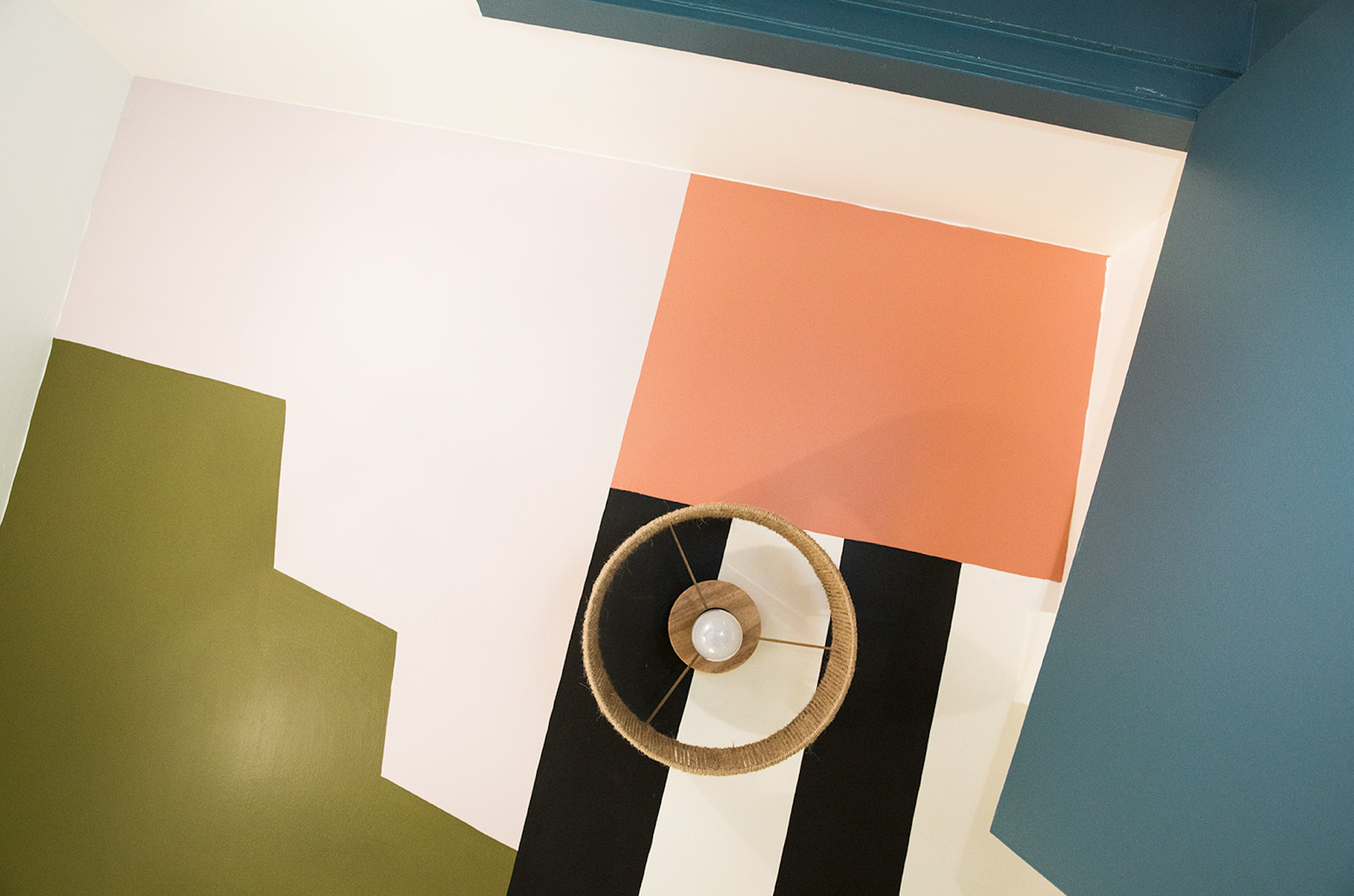 Colorful interior ceiling with geometric color blocks in white, peach, green, blue, and black, featuring a modern circular hanging light fixture.