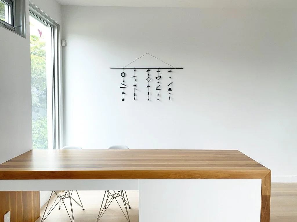 Minimalist dining area with a wooden counter, white chairs, and a wall decor featuring hanging ornaments.