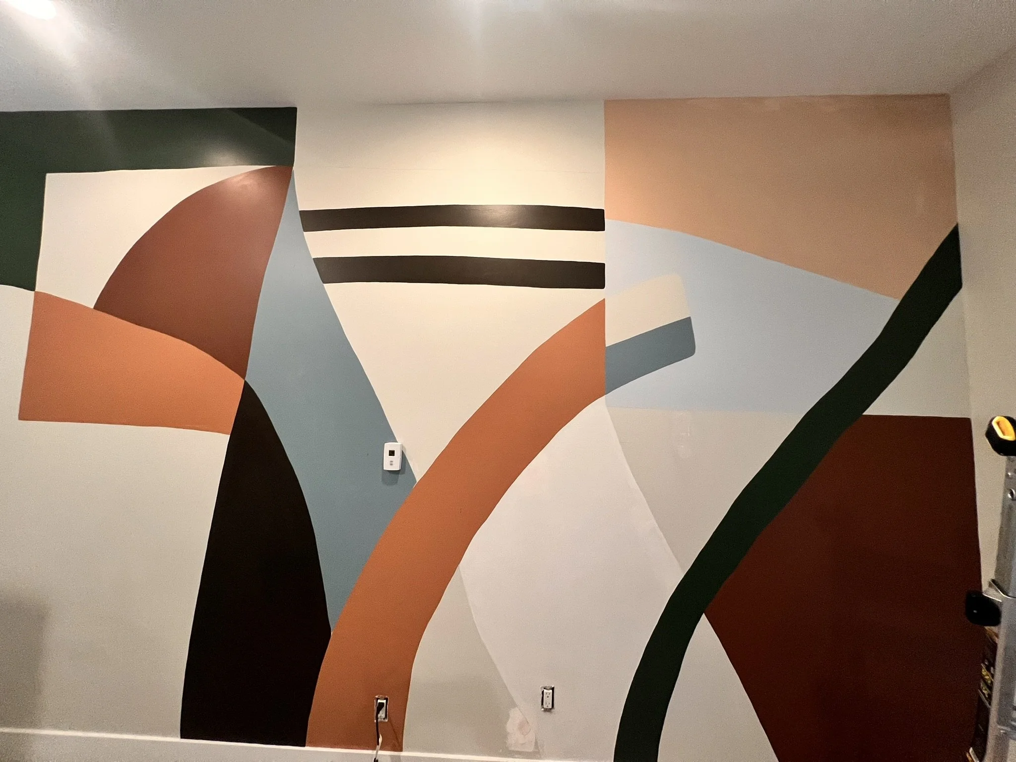 A colorful abstract mural with curved shapes in earth tones, black, white, and shades of blue, peach, and beige on a wall.