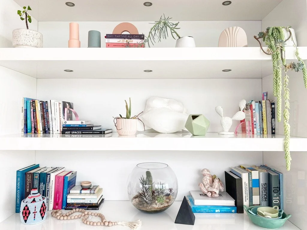 White bookshelf with various books, decorative vases, plants, and art objects arranged on three shelves.