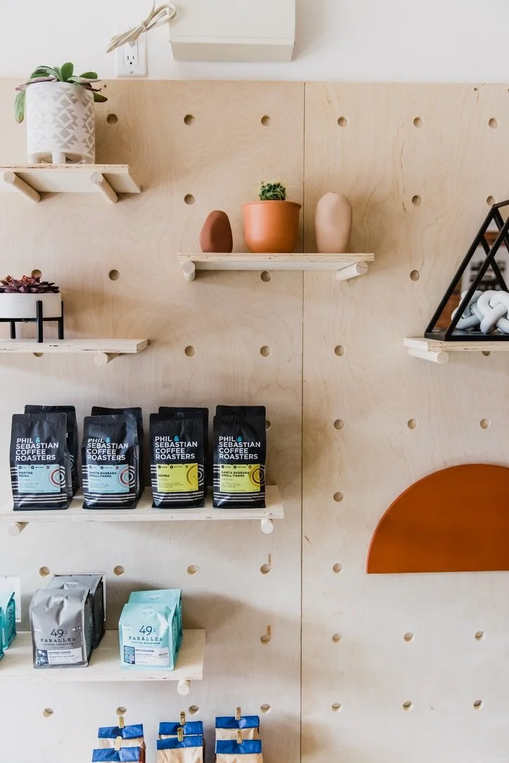 Interior  pegboard wall with wooden shelves holding potted plants, coffee bags, and accessories. Commercial coffee shop design.