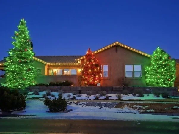 Green and red tree wraps with warm white roofline lights on a ranch home