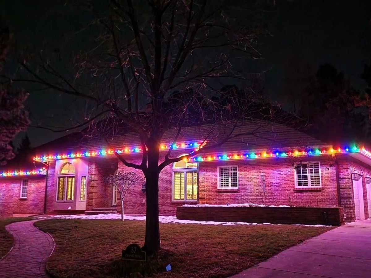Multicolor permanent roofline lights on a brick home at night