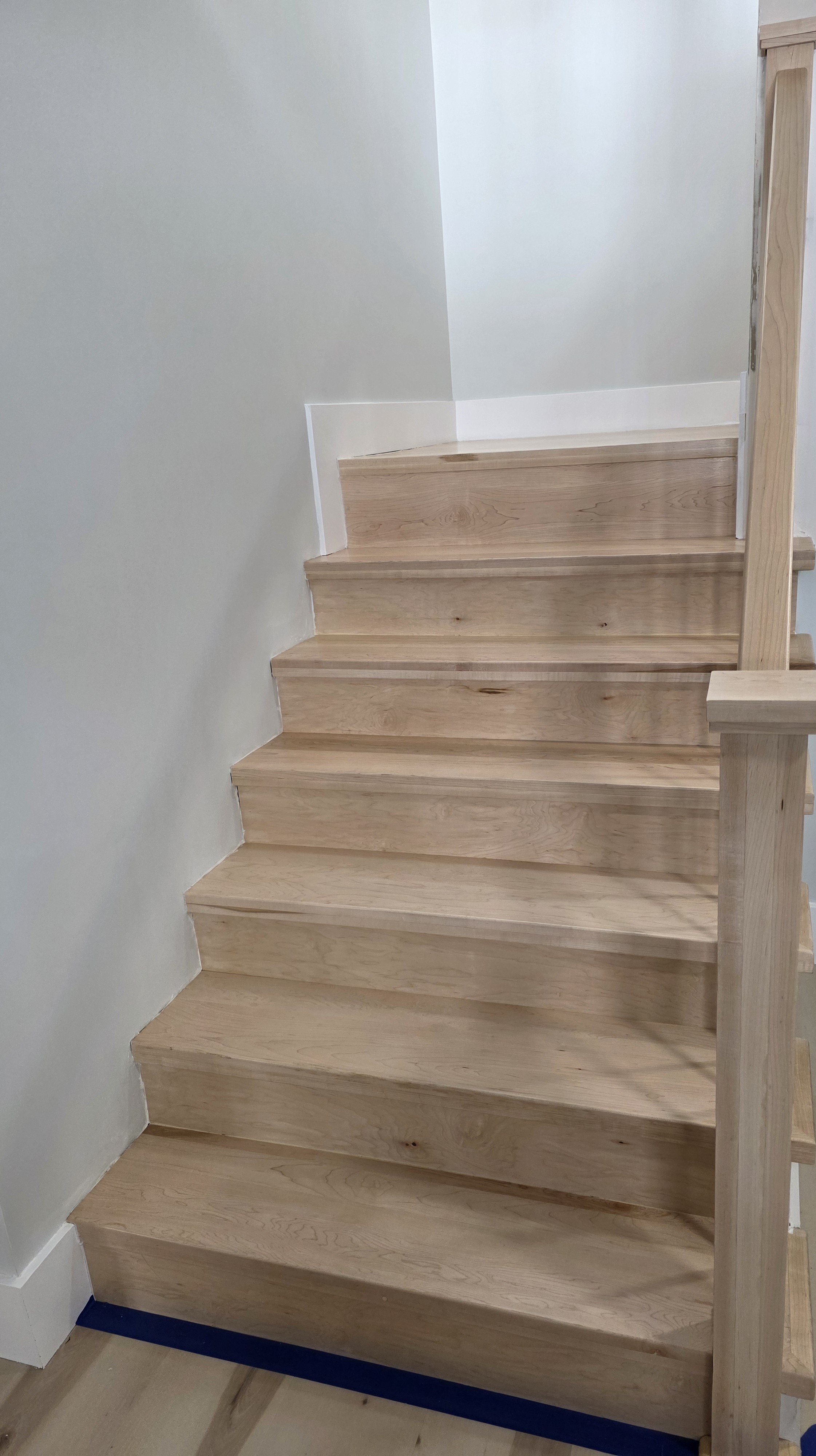 Interior view of a staircase with wooden steps and a wooden railing, with white walls.