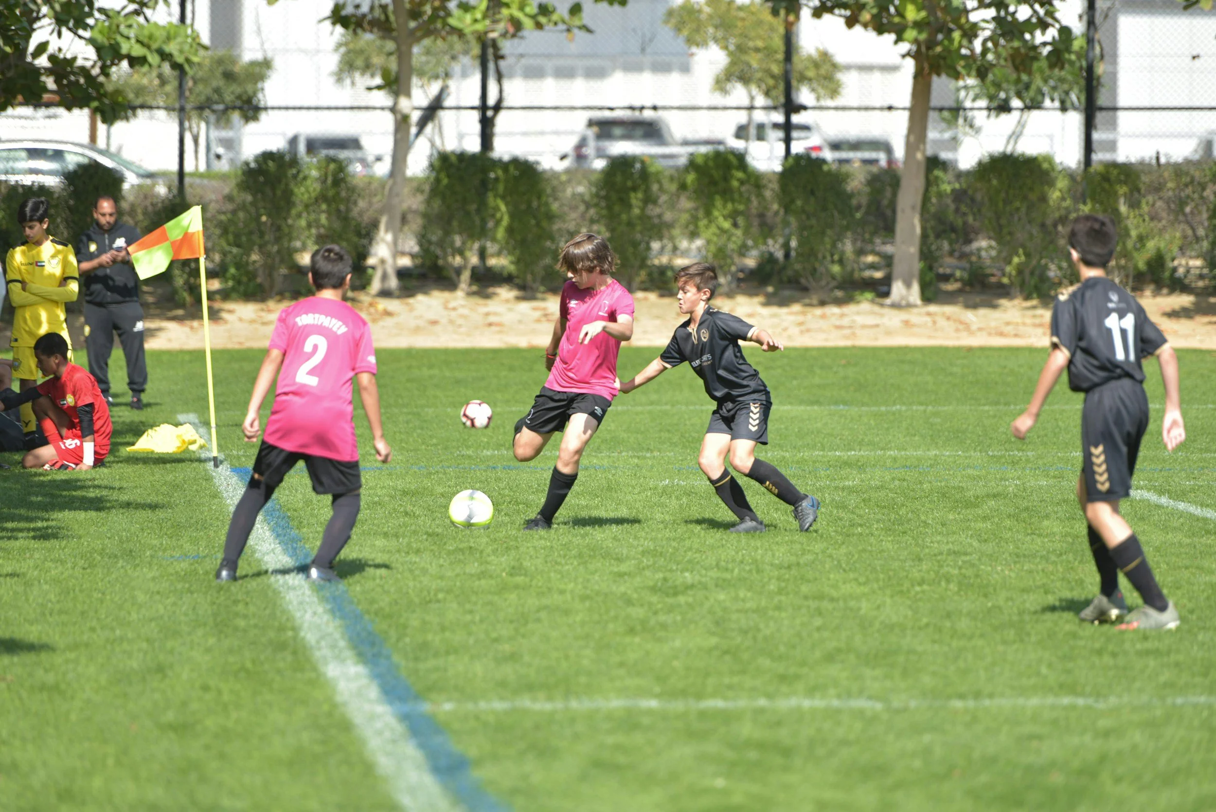 Youth soccer players competing on a sunny outdoor field near the corner flag.
