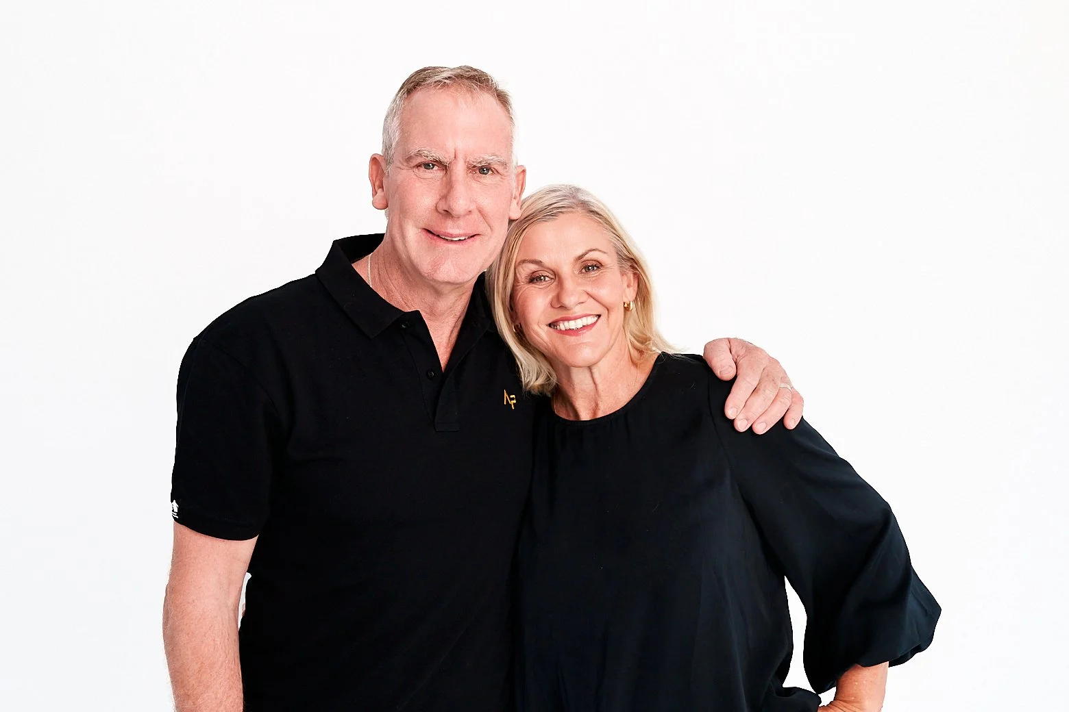 Smiling middle-aged couple in black clothing posing together against a white background