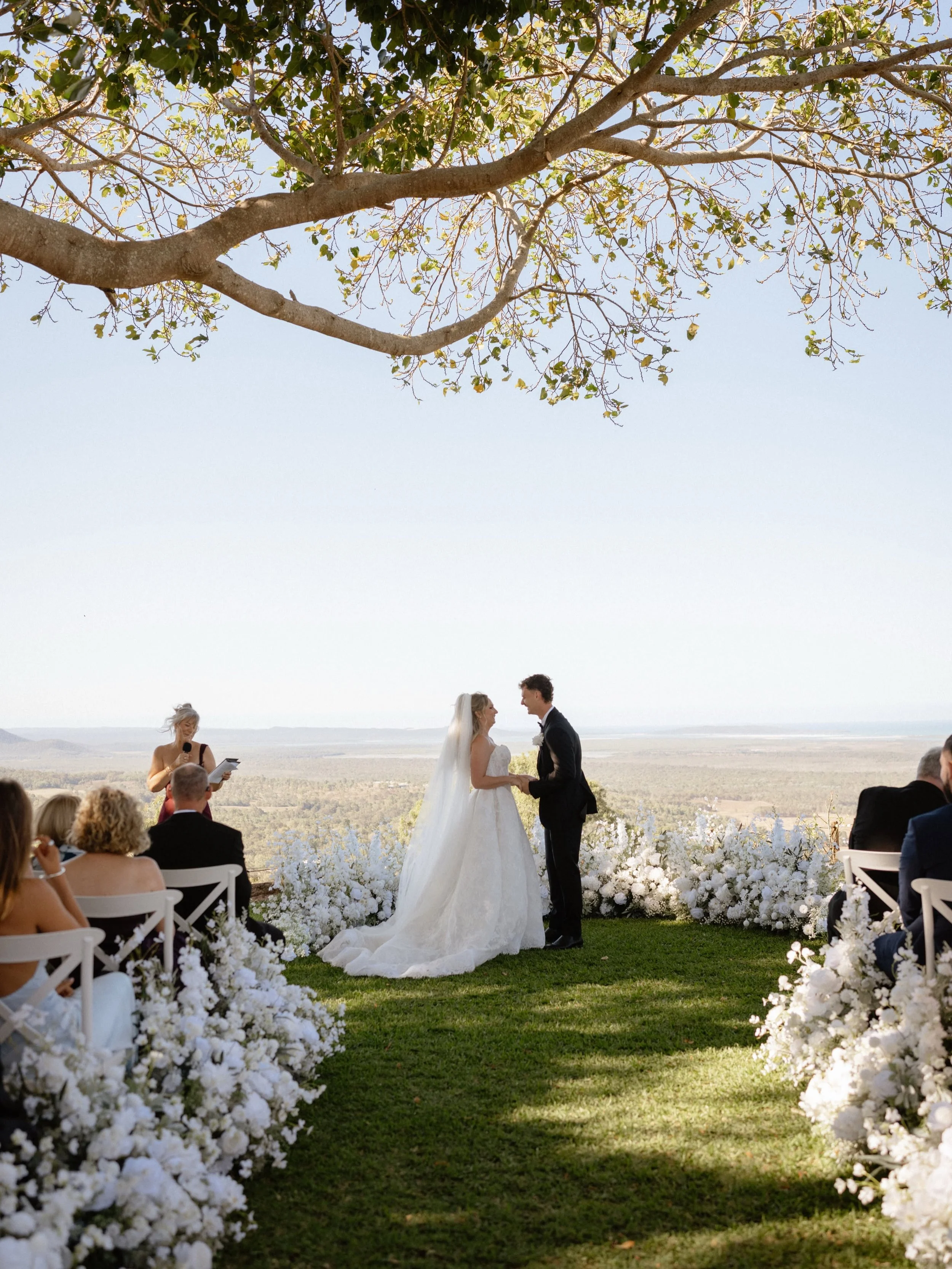 Outdoor wedding ceremony at The Lookout Woodbury on Queensland's Capricorn Coast, with the couple exchanging vows and their celebrant beside them.