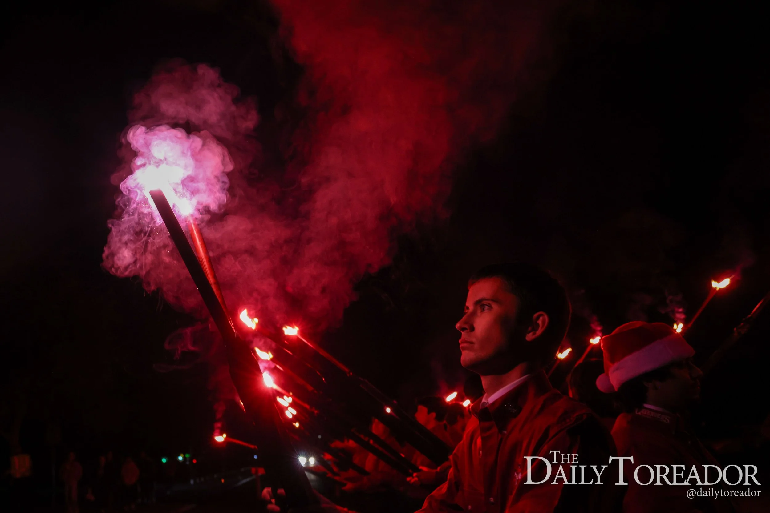 Person holding a lit flare emitting pinkish smoke at night.
