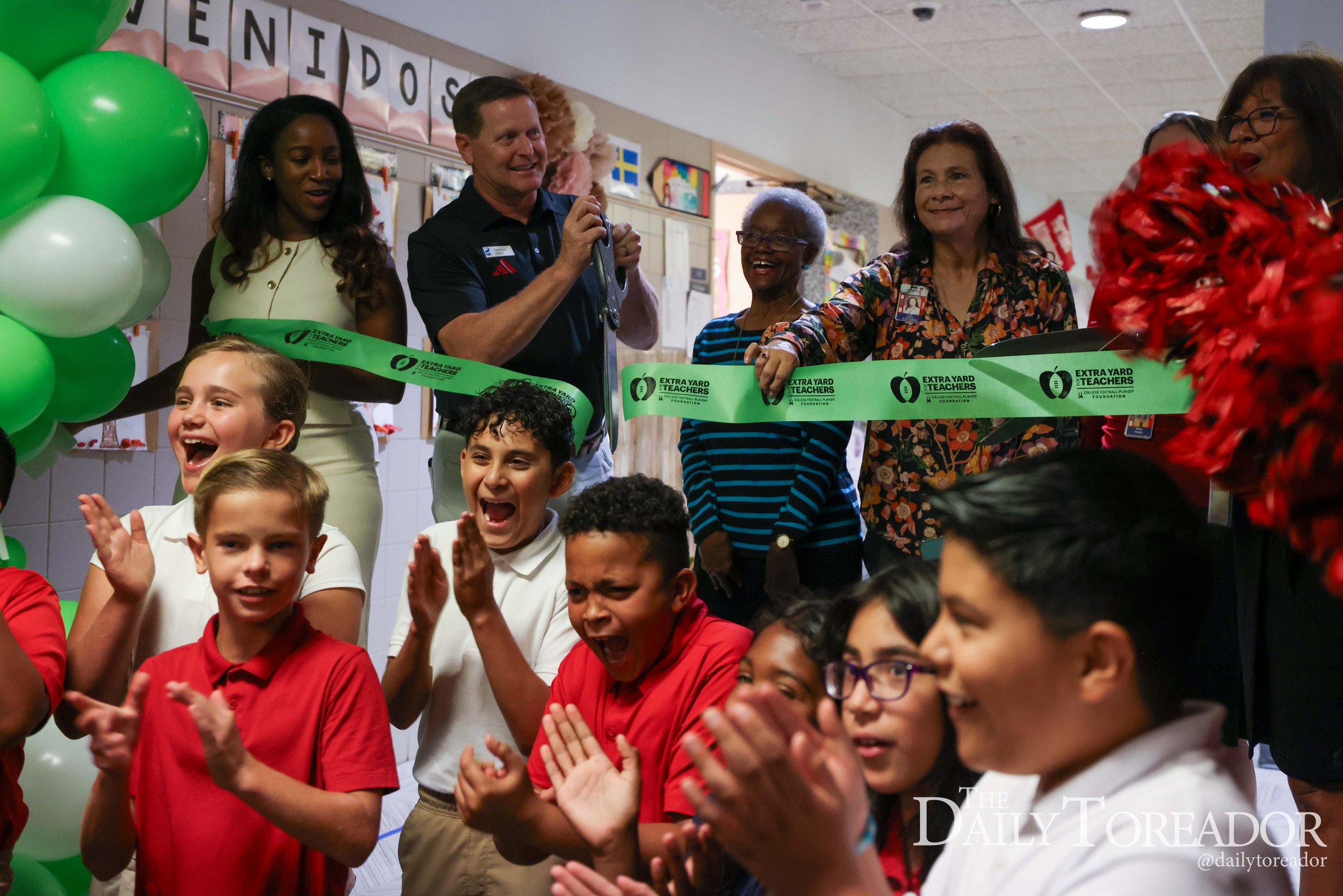 Children and adults celebrating at a ribbon-cutting event, with green balloons and smiling faces.