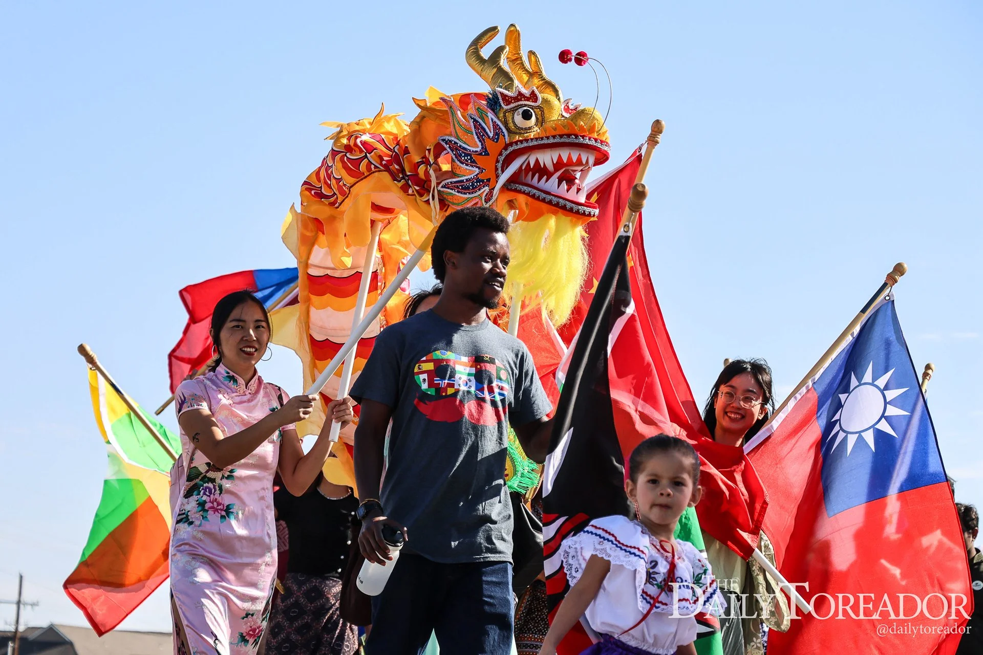 People participating in a parade with flags and a large, colorful Chinese dragon costume, under a clear blue sky.