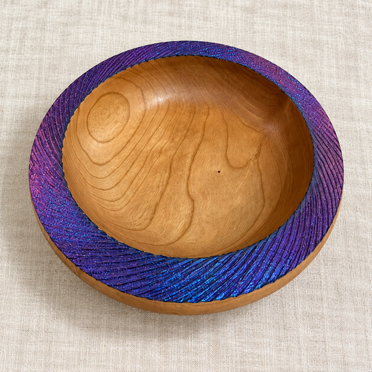 Handmade Cherry bowl on warm linen showing natural timber grain and a purple-blue textured rim