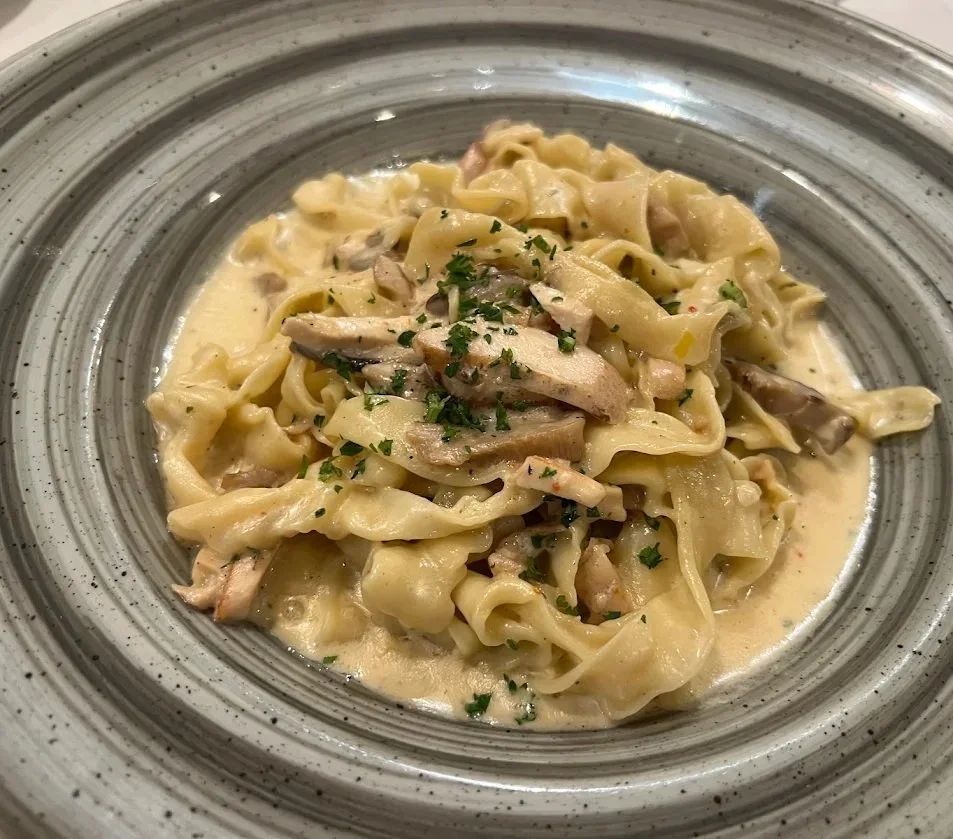 Creamy pasta with shredded chicken and herbs on a speckled ceramic plate.