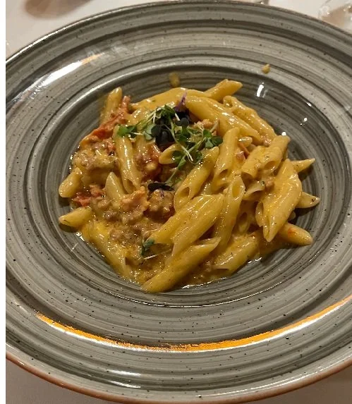 A plate of cooked pasta with creamy sauce, garnished with microgreens.