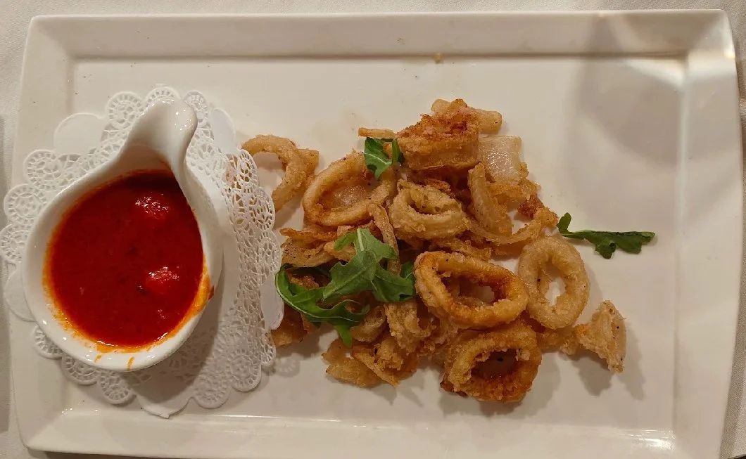 Fried calamari with marinara sauce on a white rectangular plate garnished with greens.