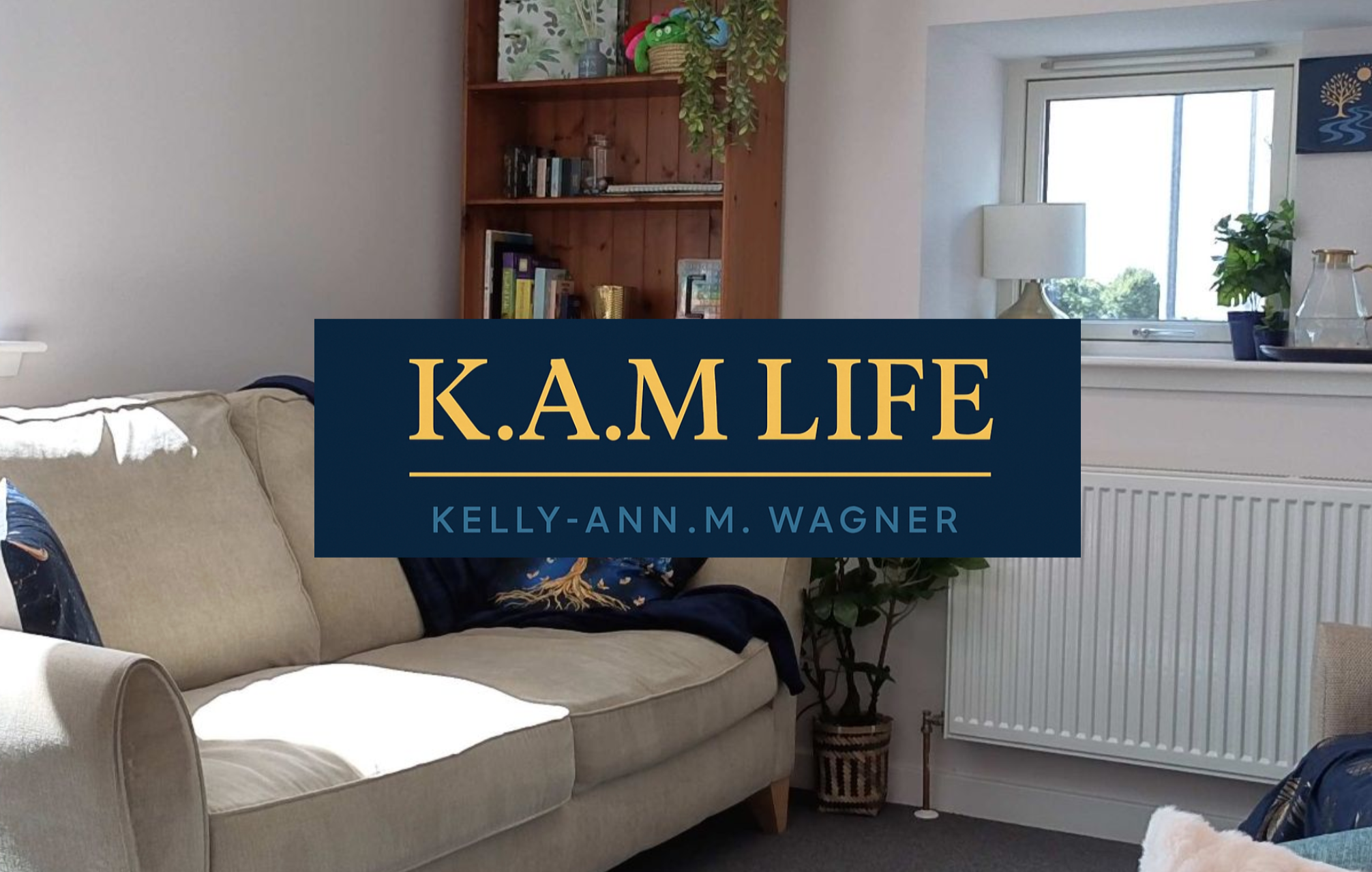 Living room with beige sofa, white wall, wooden bookshelf with decorations, plants near a window, and a beige table lamp.