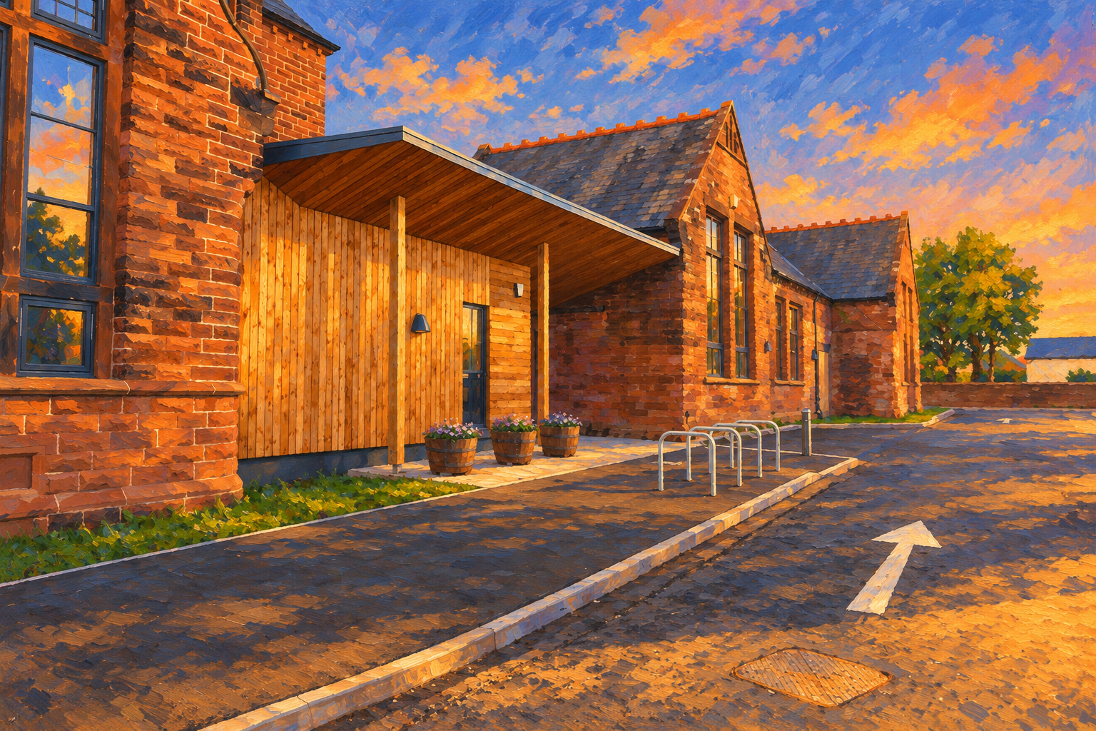 A brick building with large windows at sunset, with a wooden entrance porch featuring potted flowers, bicycles racks, a bike lane with an arrow, and a tree in the background.